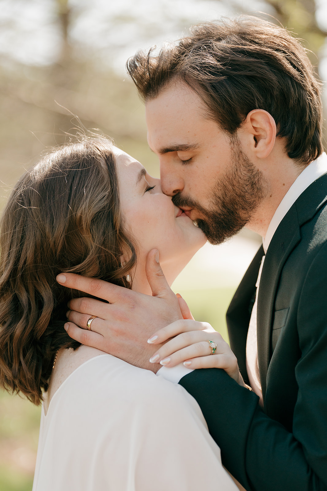 Close-up of bride and groom kissing in soft natural light with both wedding rings visible against her cape dress