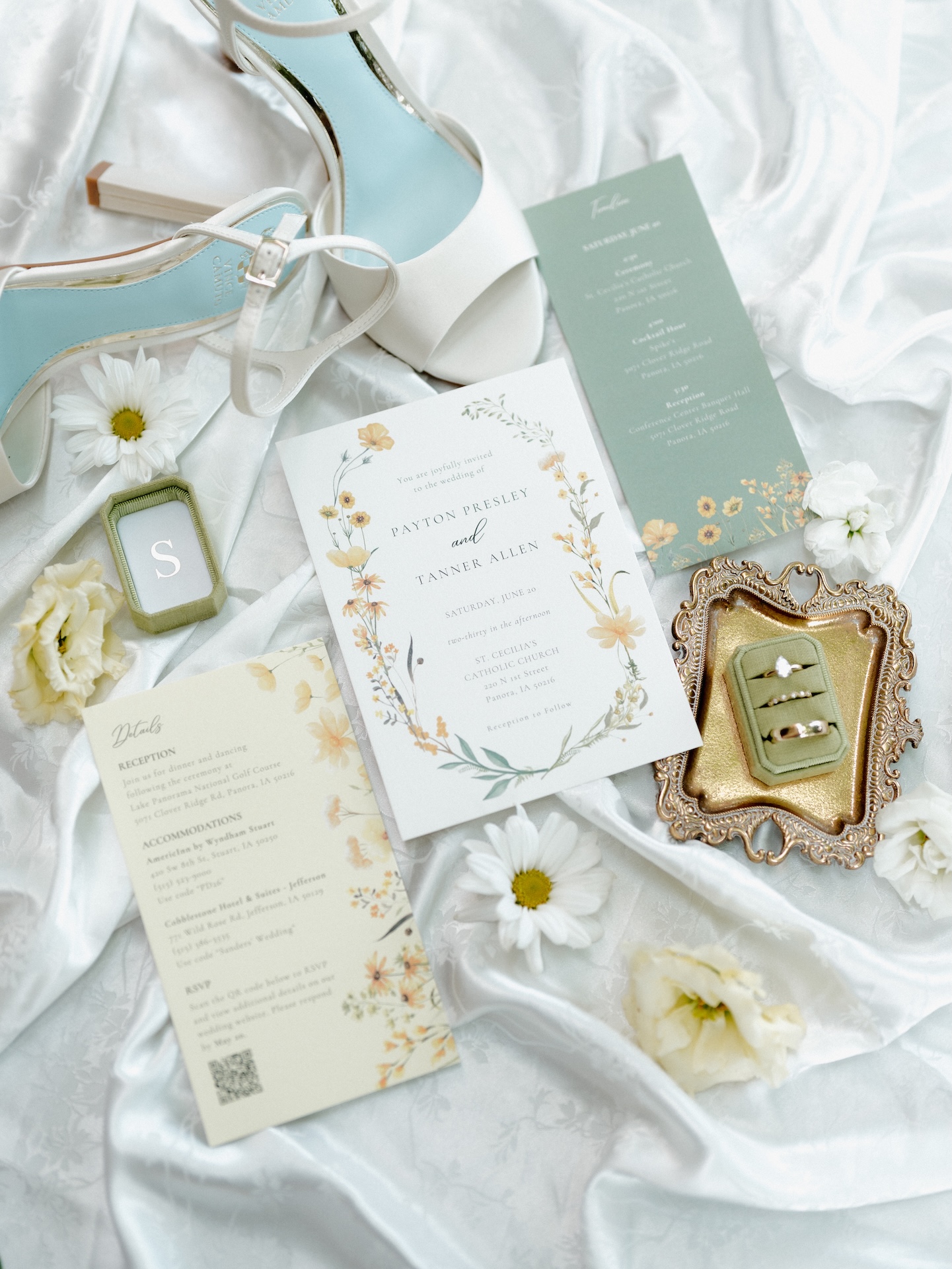 Flat lay of wedding details including a floral invitation suite for Payton Presley and Tanner Allen, white heels, vow books, wedding rings, and daisies, from a wedding with yellow bridesmaid dresses
