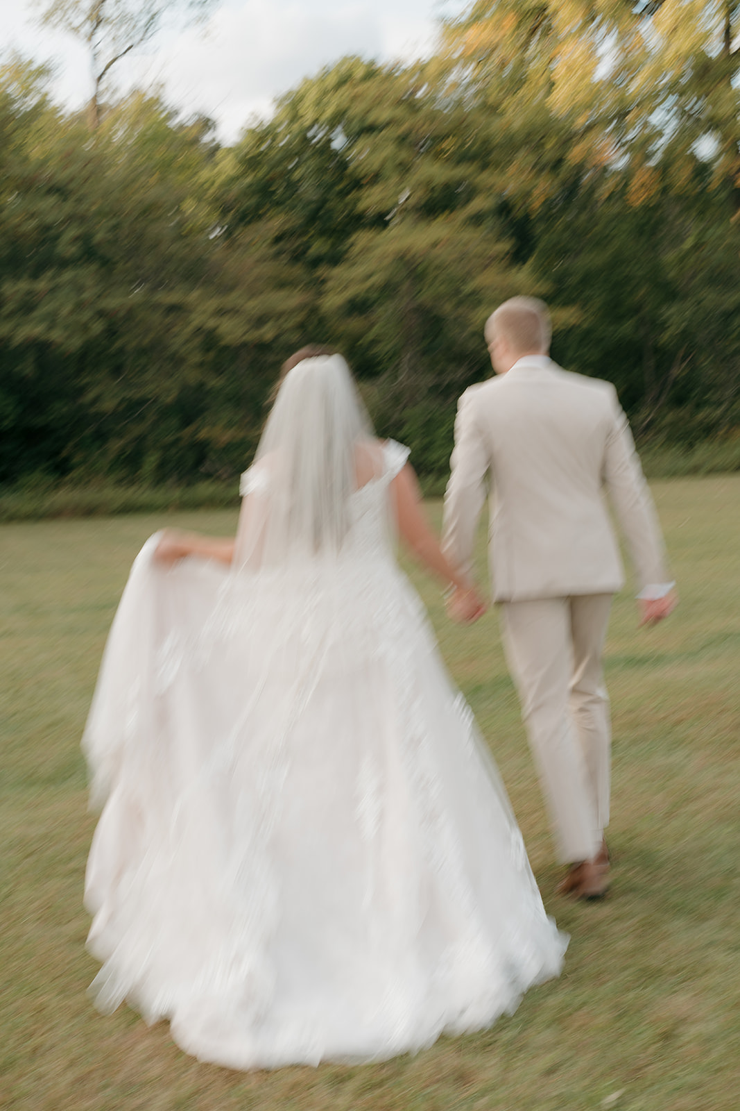 Motion blur shot of bride and groom walking hand in hand across a grassy field