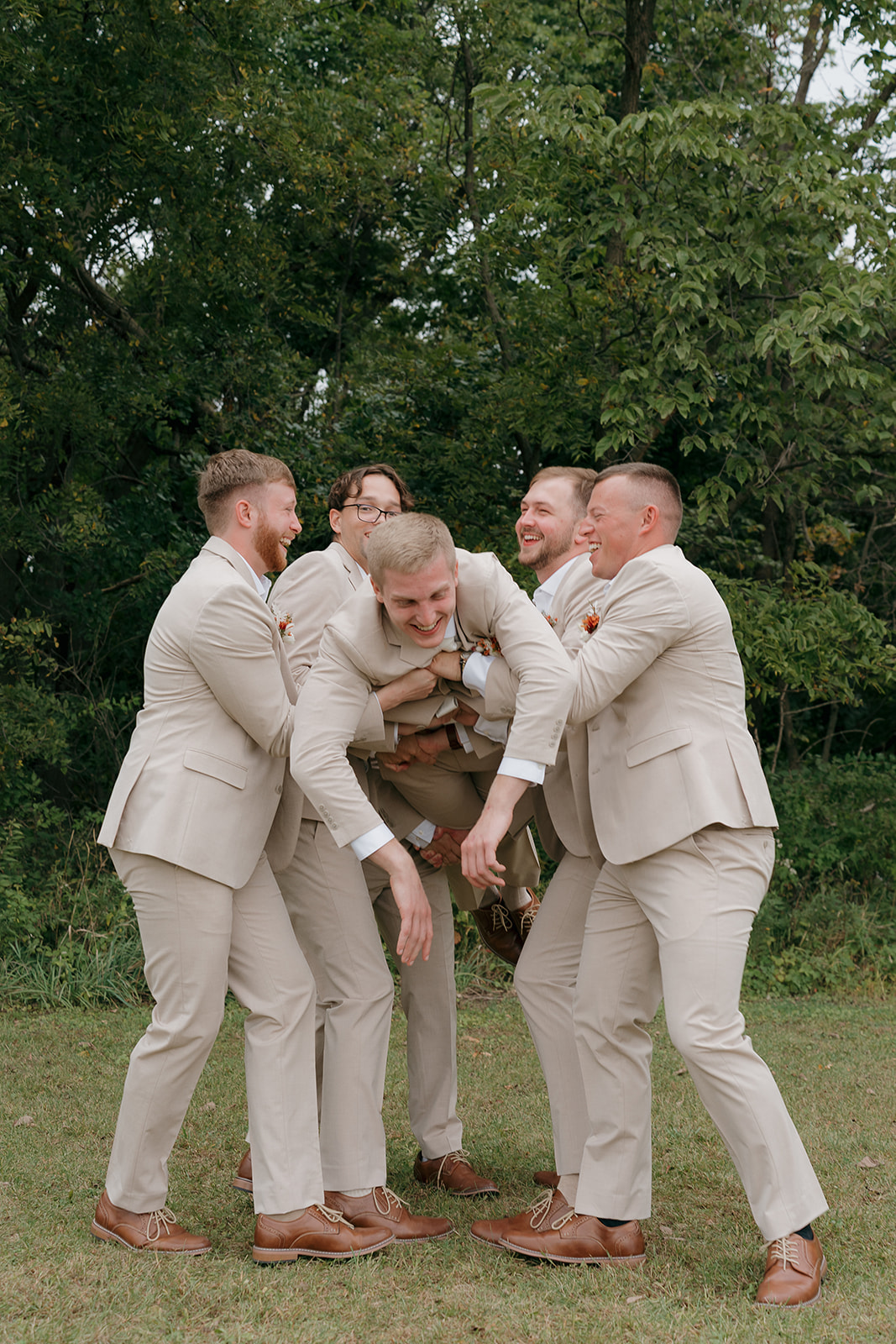 Groomsmen laughing together in tan suits in a playful group huddle in fall wedding colors