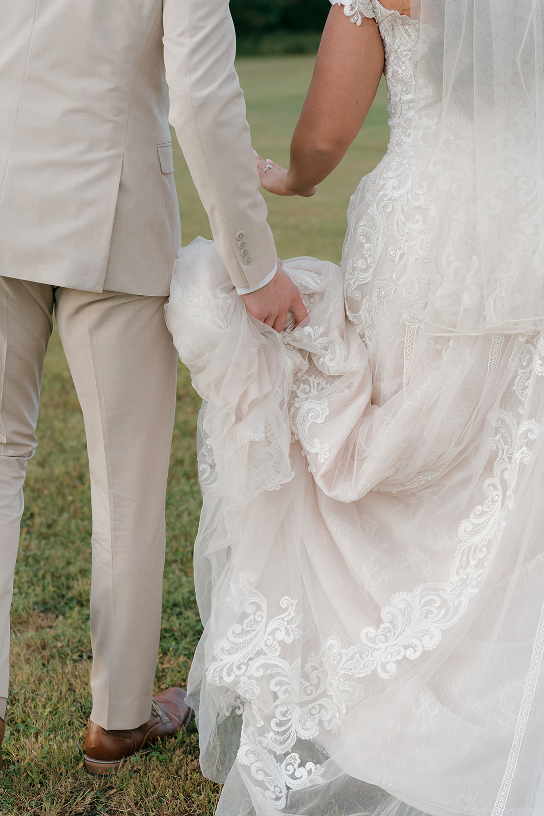 Close-up of groom holding his bride's lace gown in fall wedding colors as they walk together