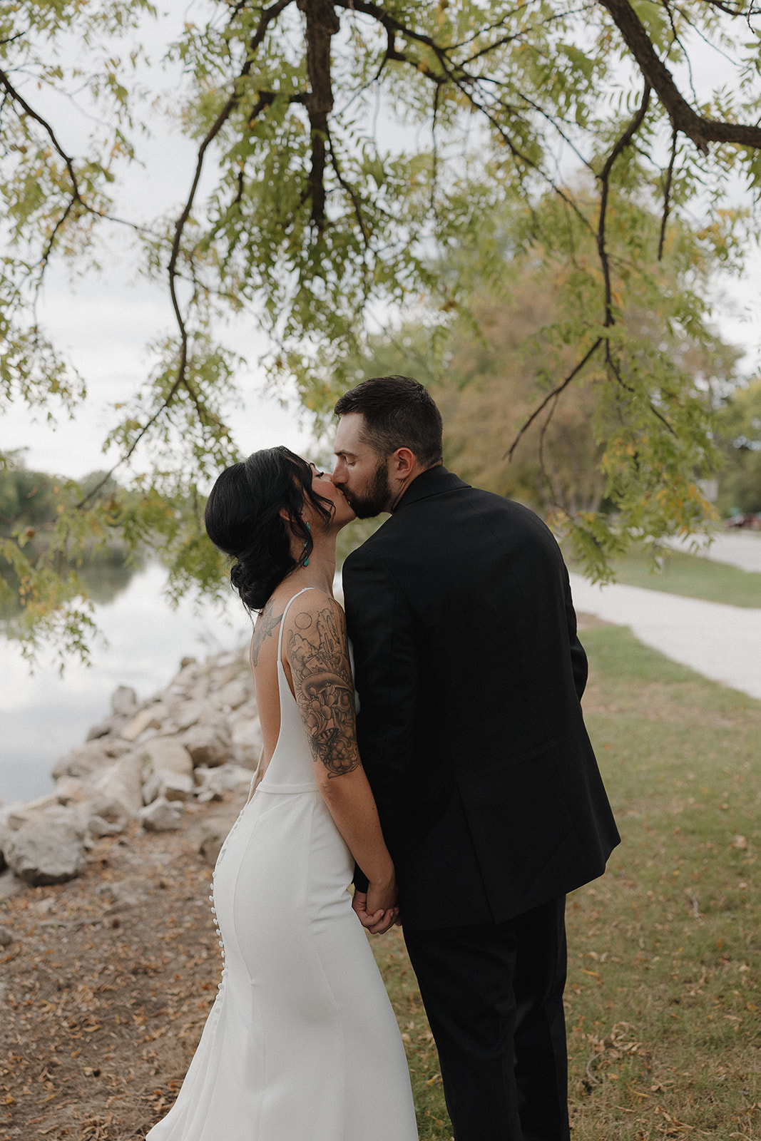 Bride and groom kissing beside a lake under hanging tree branches