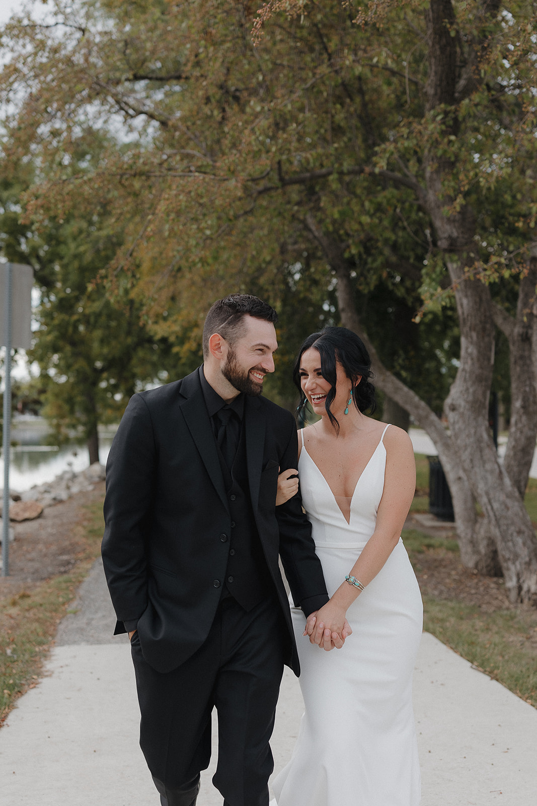 Bride and groom laughing together on a tree lined path near the water