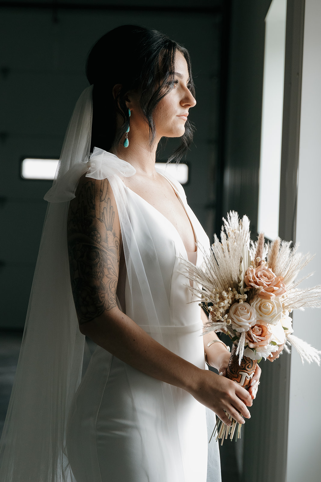 Bride in profile wearing turquoise drop earrings and a bow strap veil, soft window light on her fall wedding day