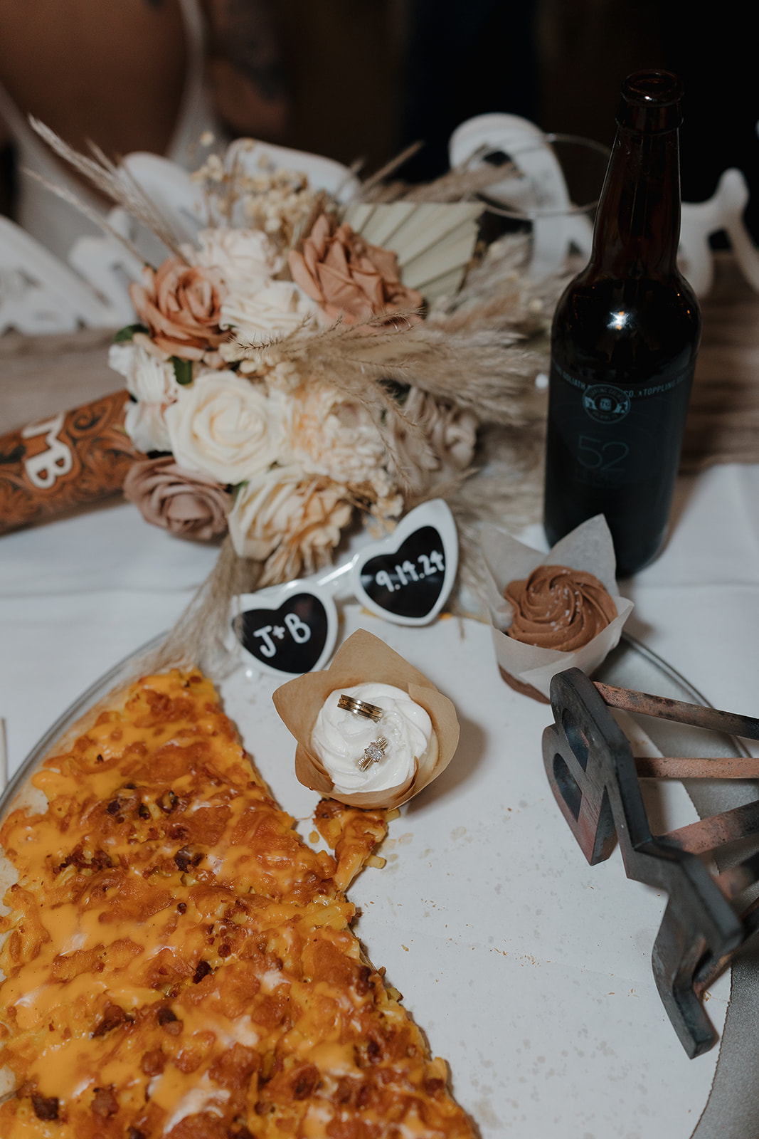 Reception table detail with pizza, heart shaped sunglasses, rings, and a craft beer bottle, cozy fall wedding vibes