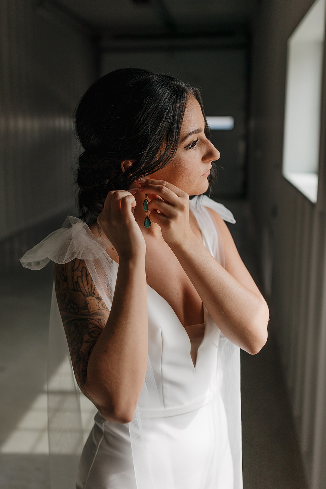 Bride fastening her turquoise earring in soft hallway light before the ceremony