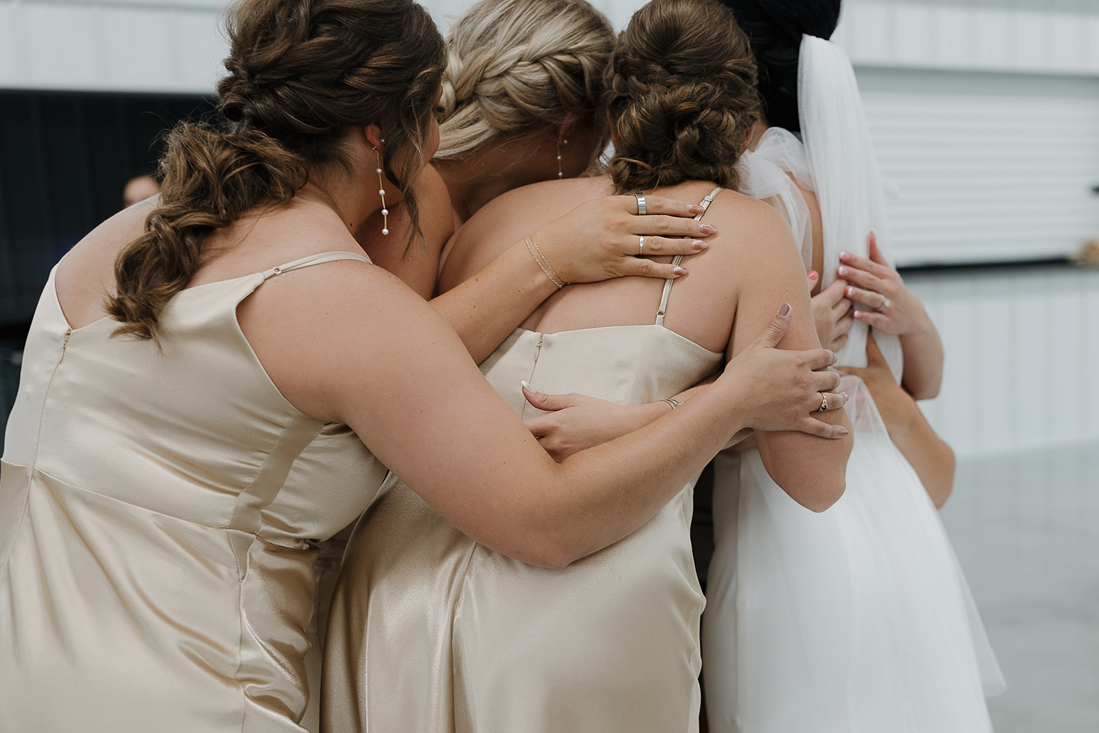 Bridesmaids in champagne satin dresses sharing a group hug before the ceremony
