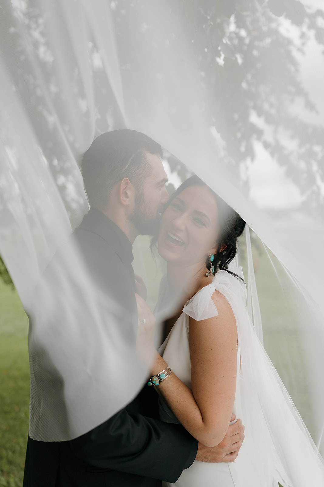 Dreamy veil shot of the bride and groom embracing, her turquoise bracelet catching the light