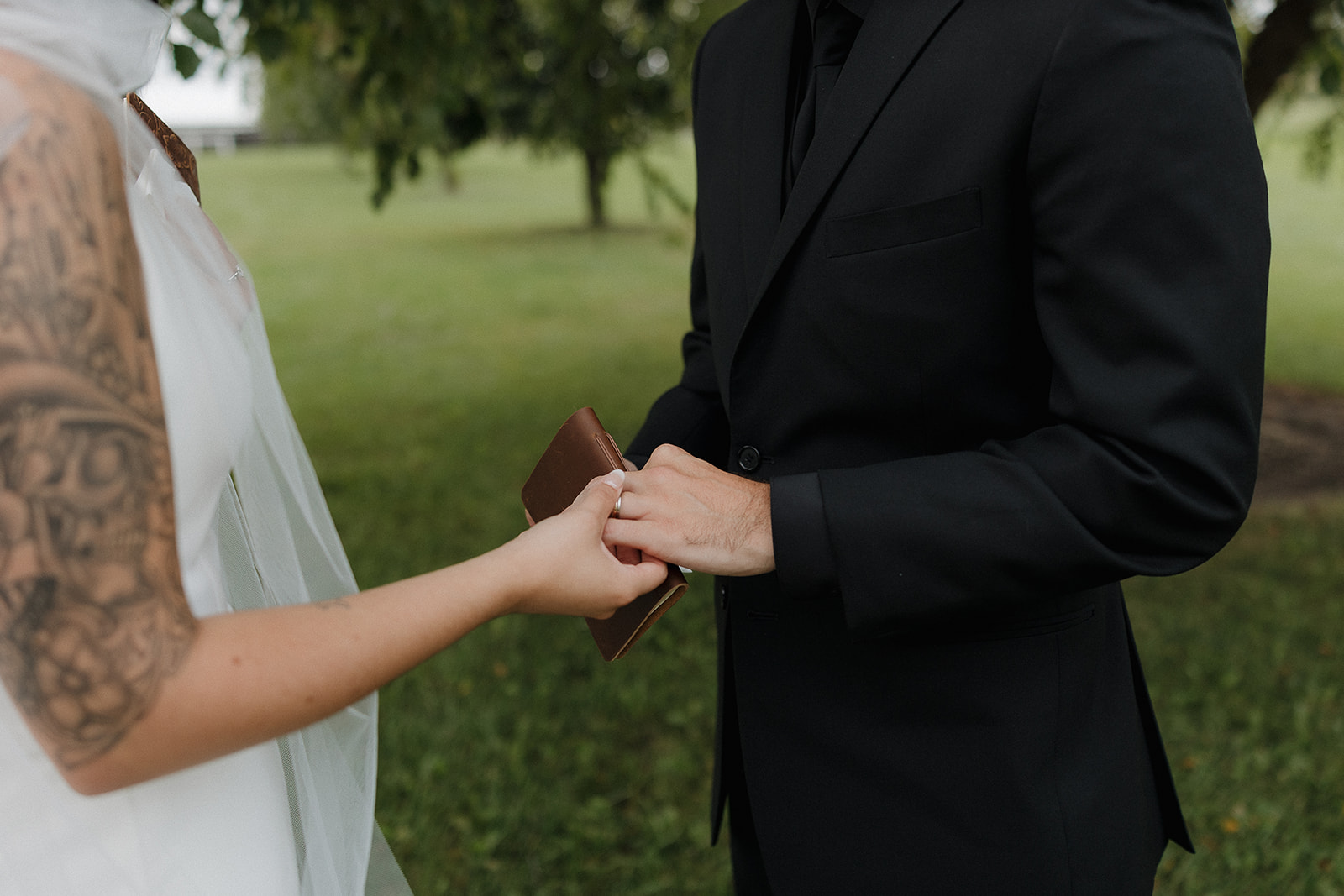 Bride and groom holding hands and exchanging vows from a small leather book