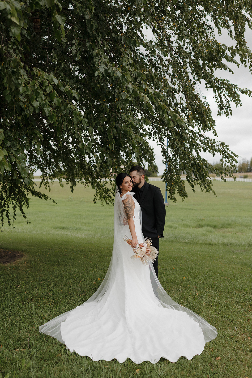Bride looking back over her shoulder with her cathedral veil pooling on the grass, a dreamy fall wedding portrait