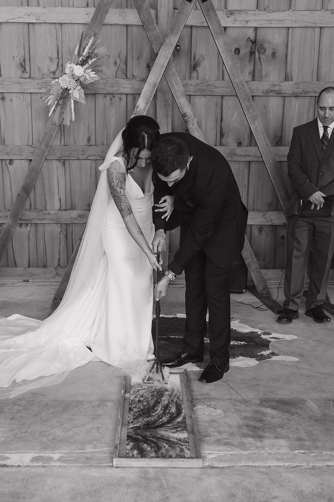 Black and white shot of the bride and groom lighting a unity sand ceremony together
