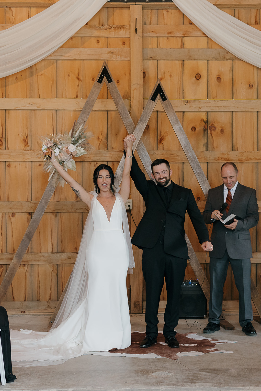 Bride and groom raising joined hands in celebration after their ceremony under a wooden mountain arch