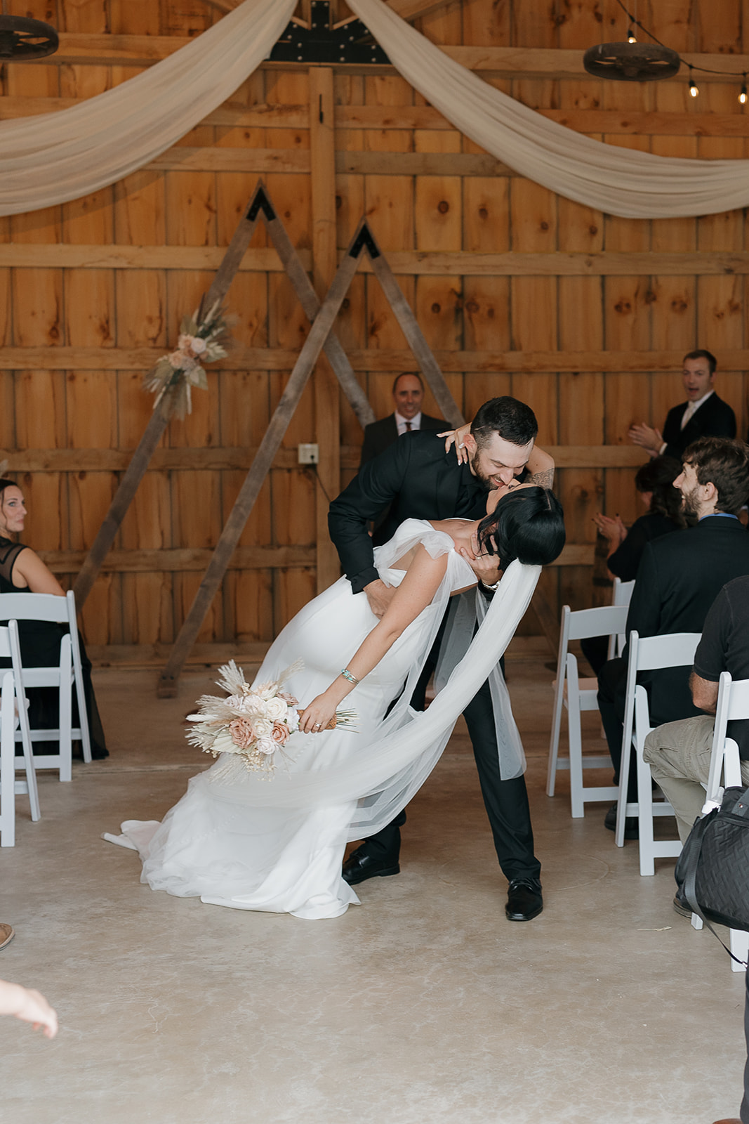 Groom dipping the bride for a kiss as guests cheer at the end of their barn ceremony