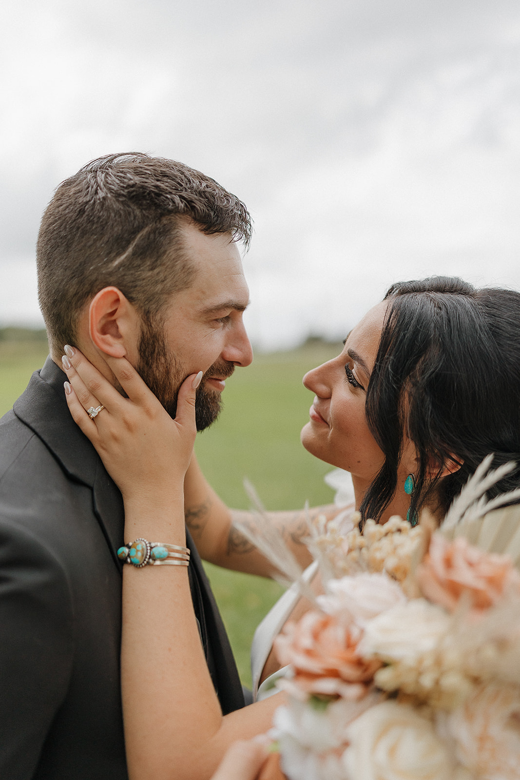 Close up of the bride cradling the groom's face, her bouquet and turquoise jewelry in the foreground