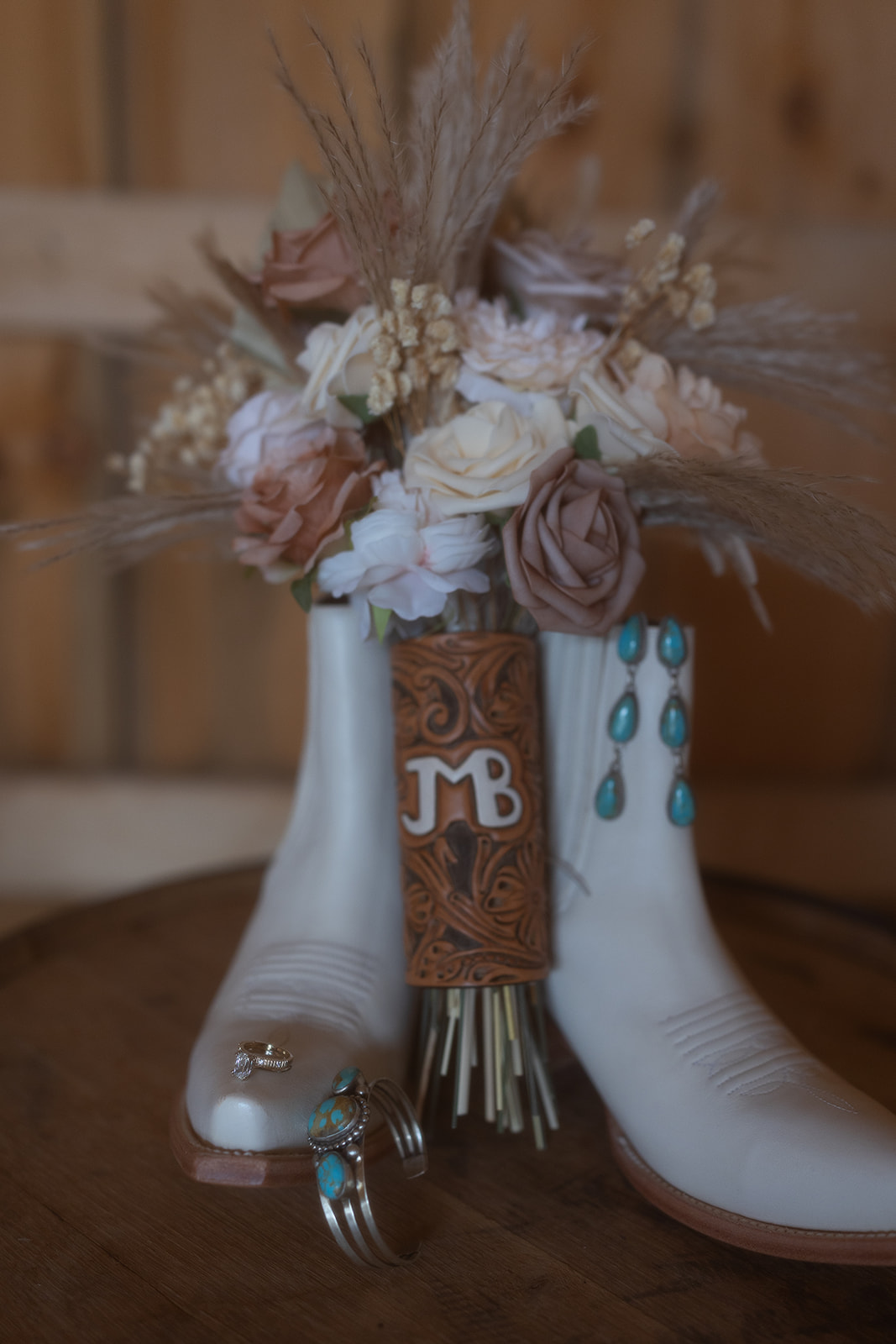 Flat lay of the bridal bouquet resting between white cowboy boots with turquoise jewelry and wedding rings