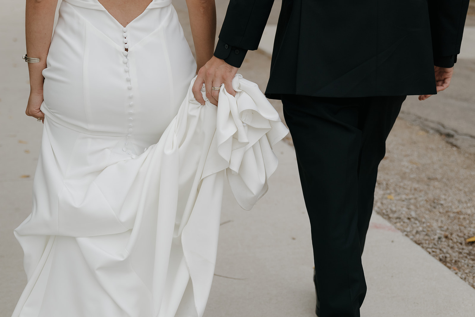 Close up of the bride's button back gown and the groom's hand holding her train as they walk