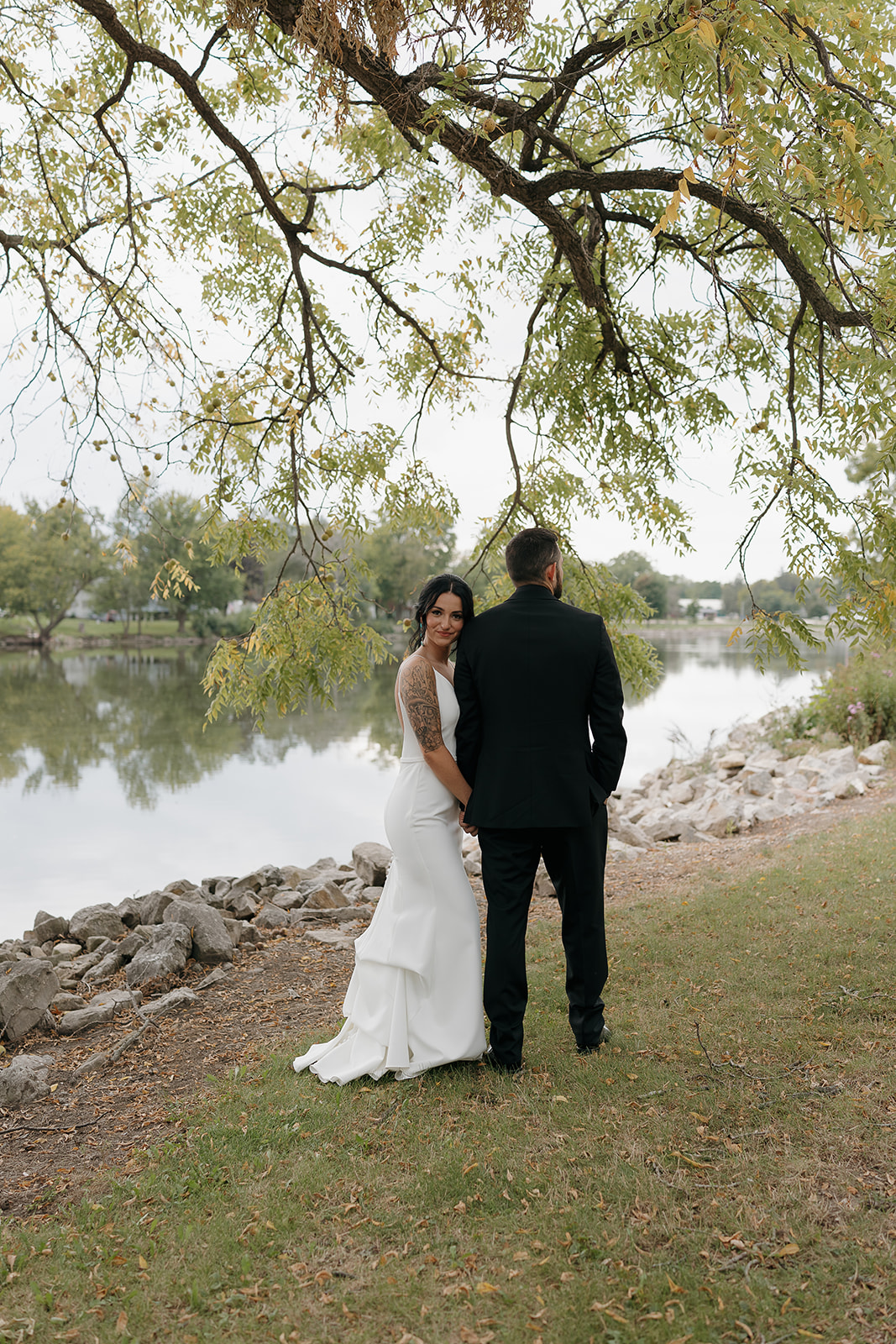 Bride glancing back over her shoulder while holding hands with the groom by the lake