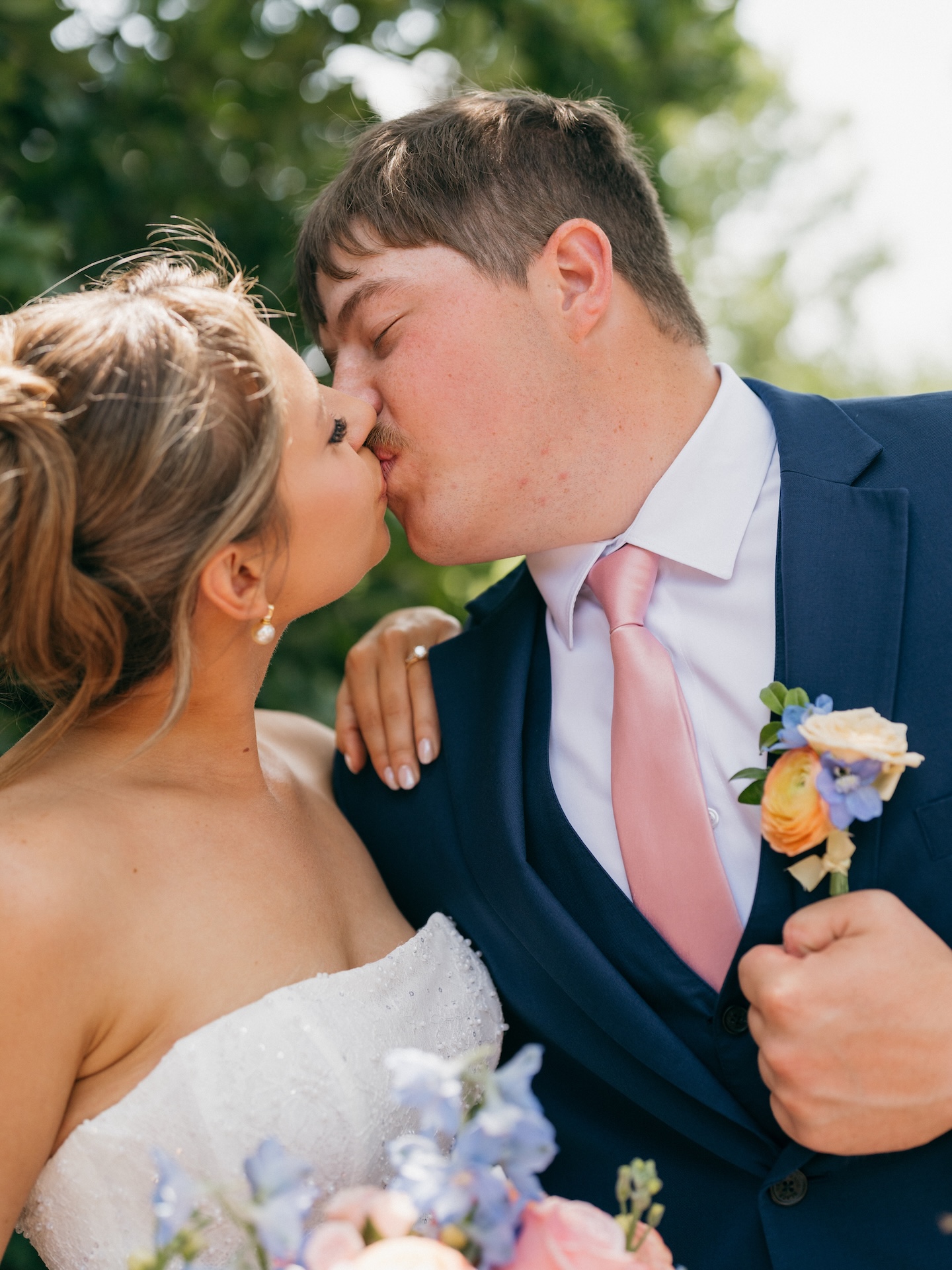 Close-up of the bride and groom kissing, showing his peach and blue boutonniere in detail.