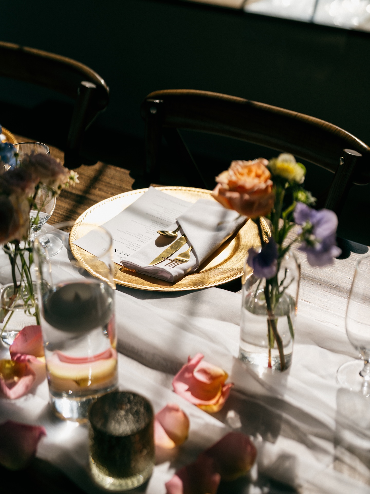 Gold charger place setting with a folded napkin, menu card, and loose garden roses on a colorful wedding tablescape.
