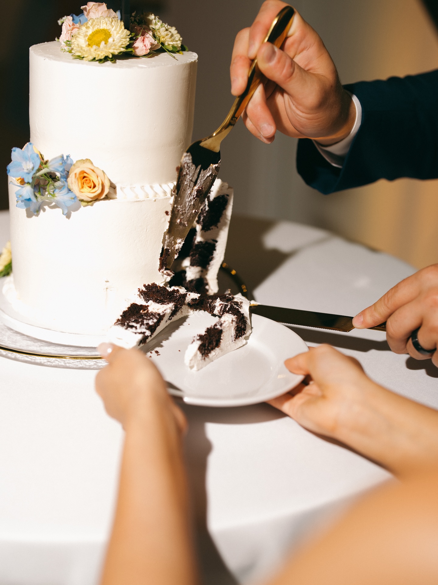 Close-up of the bride and groom cutting into their white buttercream cake topped with fresh peach roses and blue delphinium.