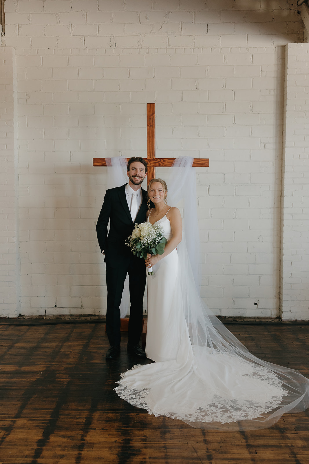 Bride and groom posing together in front of a wooden cross backdrop after their ceremony.