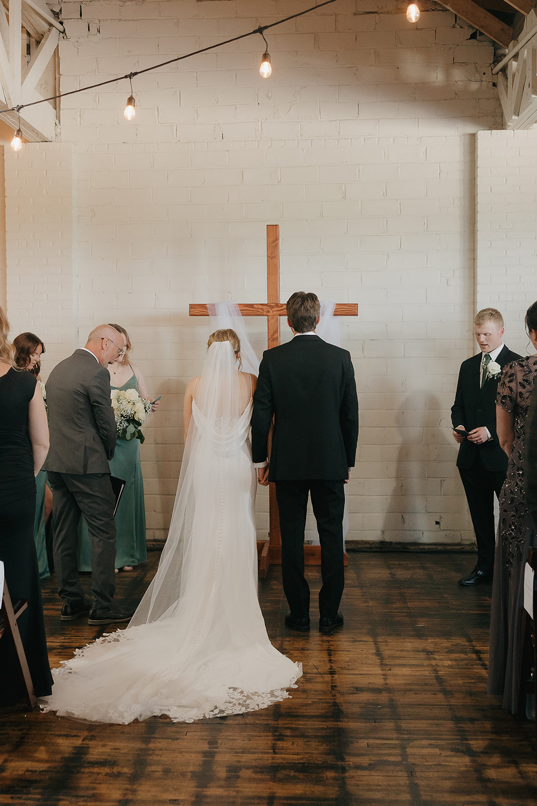 Bride and groom standing together at the altar in front of a wooden cross during their ceremony at this modern wedding venue (Highpoint Event Center).