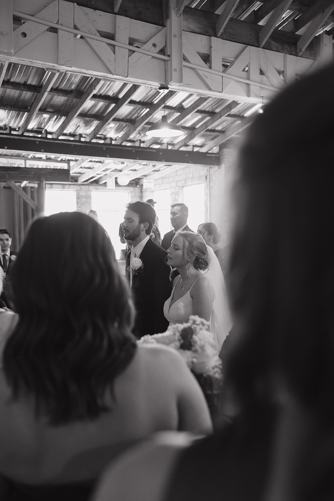 Black and white candid of the bride and groom standing together during a quiet ceremony moment.