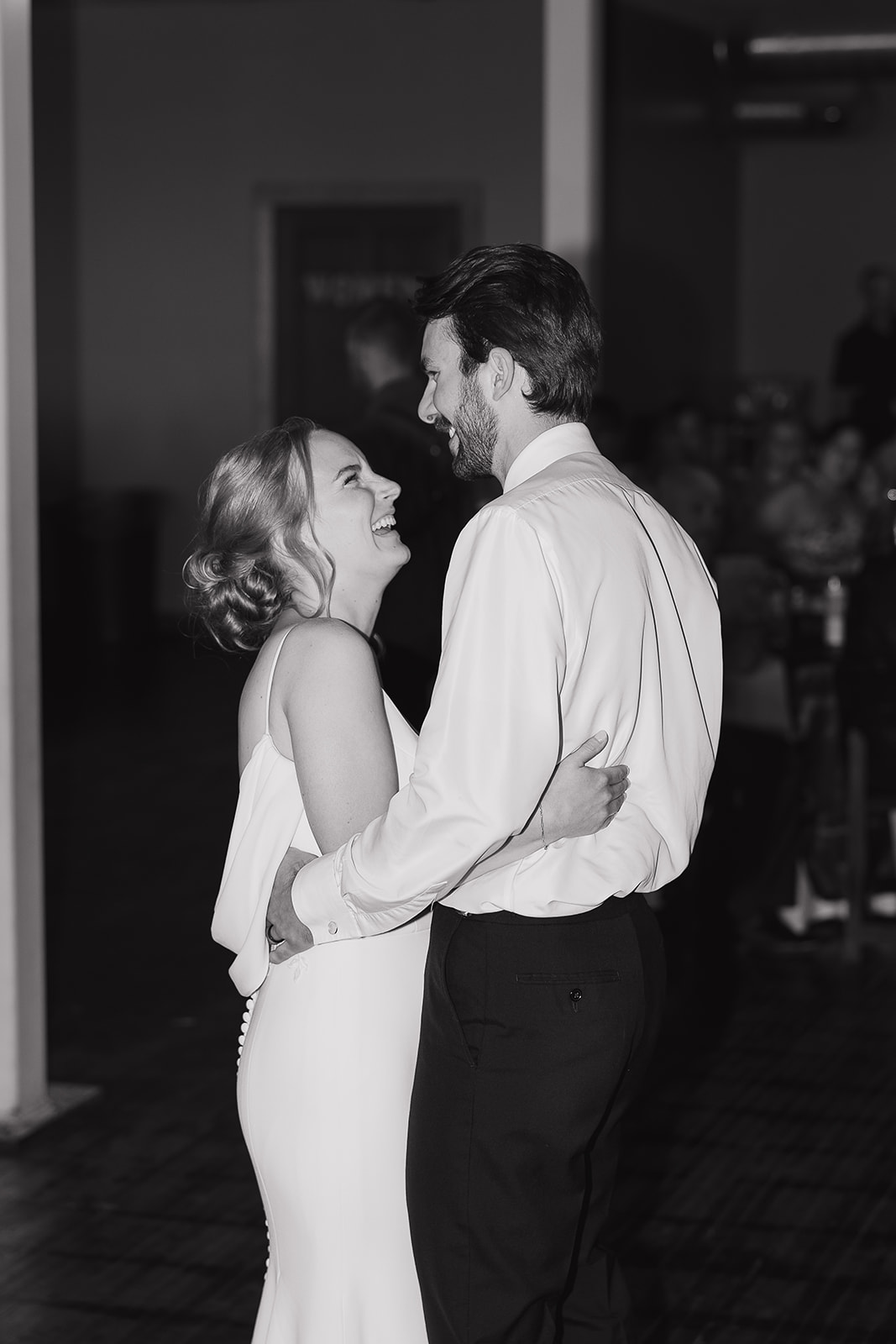 Black and white candid of the bride and groom laughing together while slow dancing at their reception.