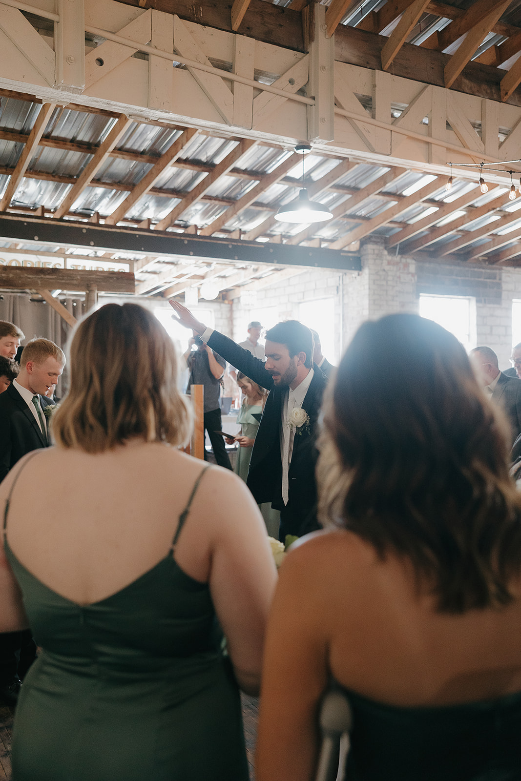 Groom raising his hand during a blessing over his bride surrounded by bridesmaids at this modern wedding venue (Highpoint Event Center).